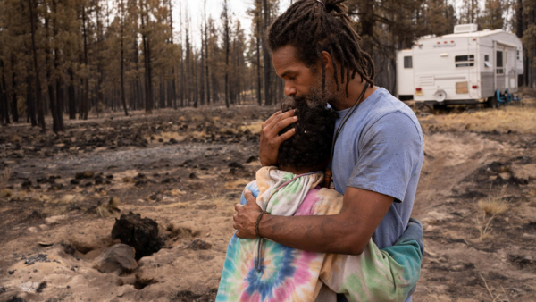 Nicolas Bey, 11, hugs his father, Sayyid Bey, within sight of a donated trailer they were using near Beatty, Ore., July 19, 2021, after their home was burned in the Bootleg Fire. (CNS photo/David Ryder, Reuters)